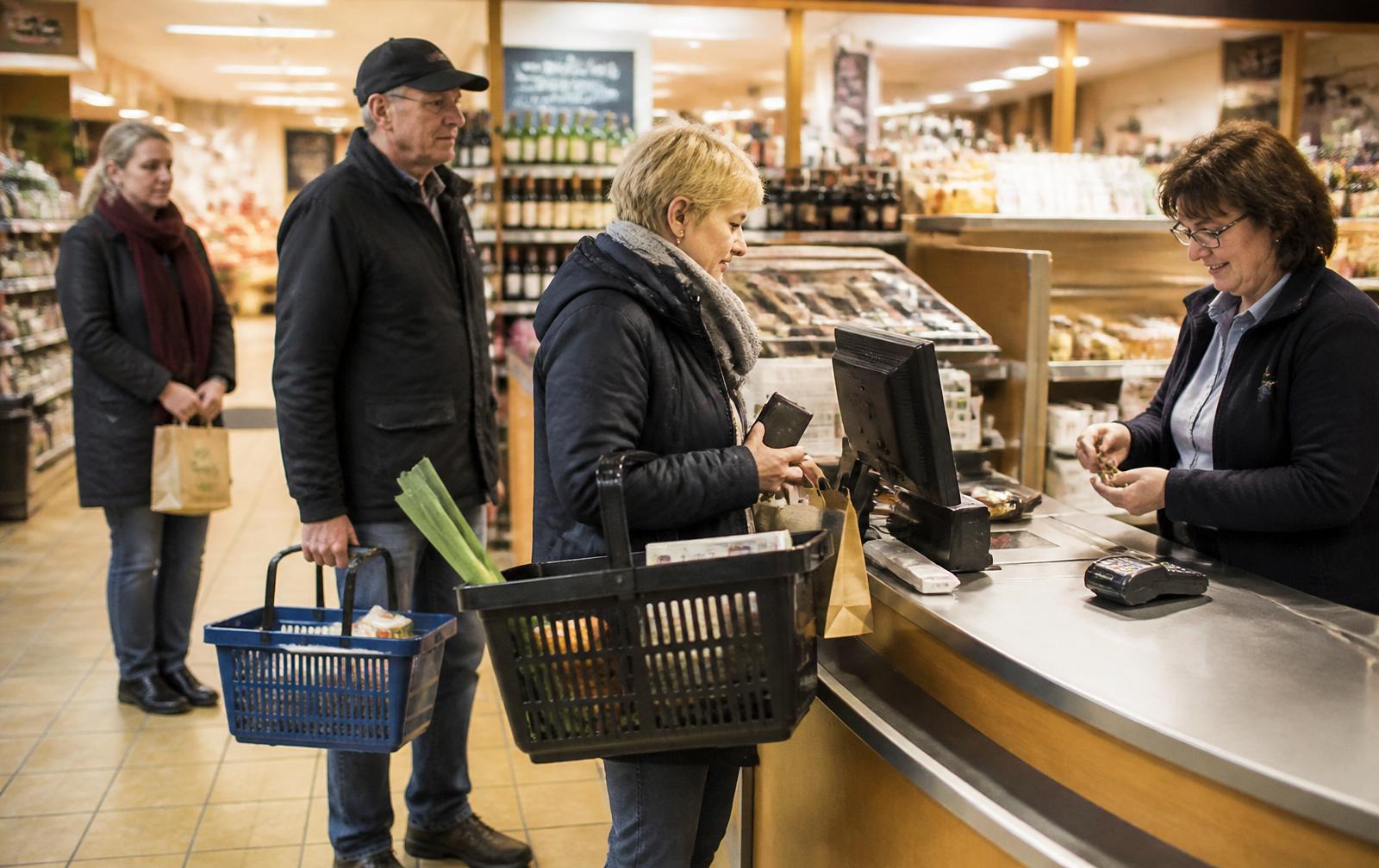 Kundinnen und Kunden warten an einer Supermarktkasse.