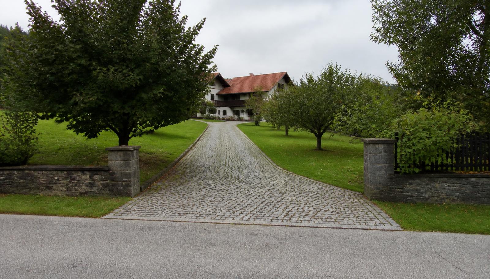 Lange gepflasterte Einfahrt von der Straße zu einem weit hinten liegenden Einfamilienhaus
