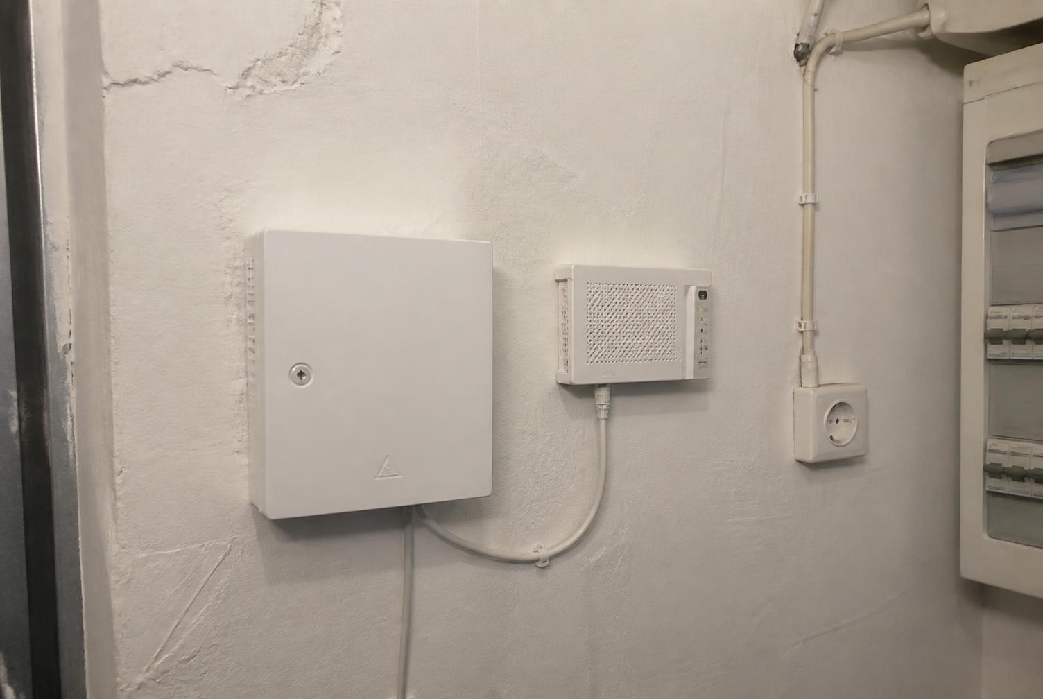 HÜP und ONT nebeneinander an einer Kellerwand mit Steckdose und Netzwerkkabel