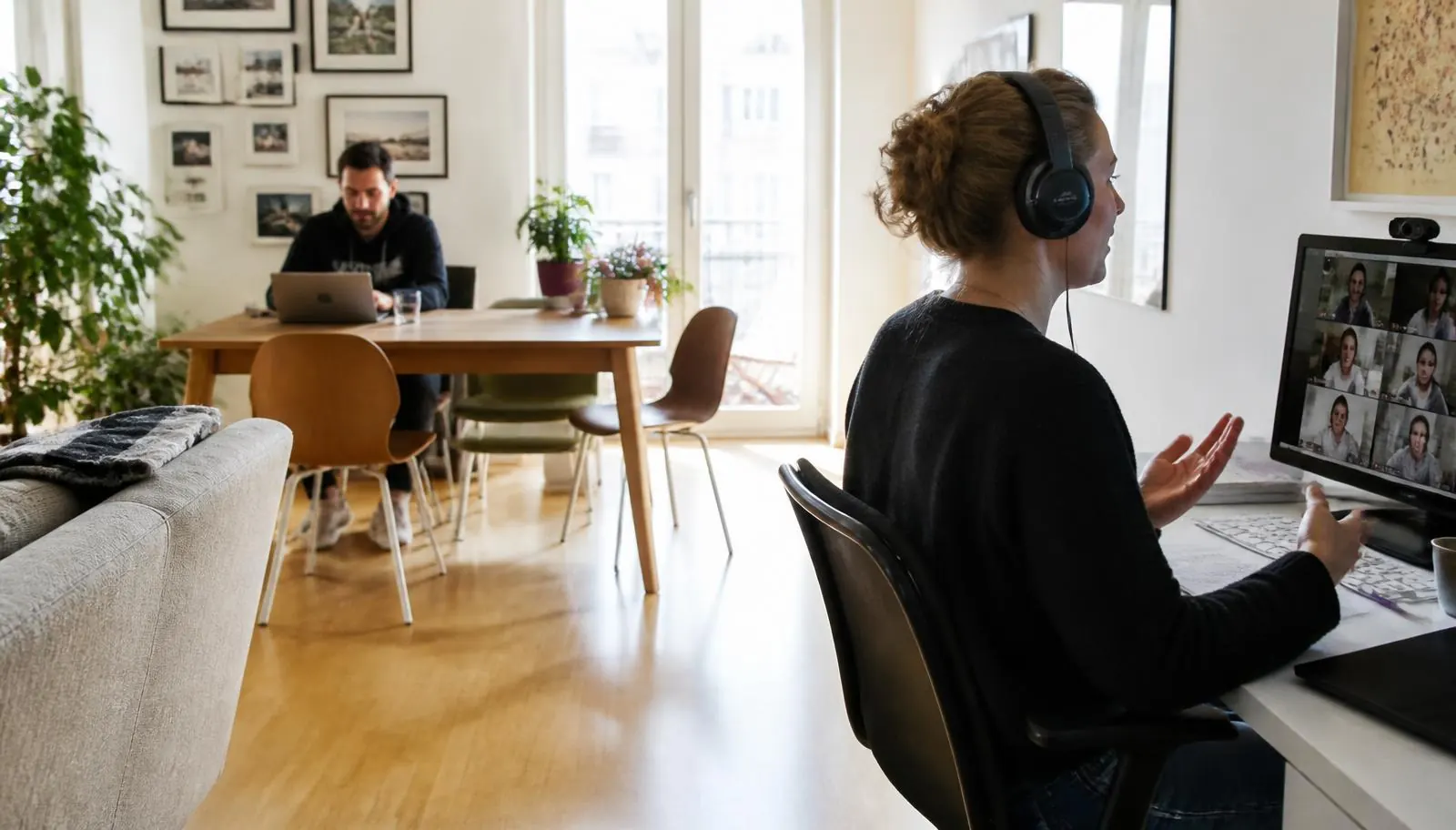 Zwei Personen arbeiten gleichzeitig im Homeoffice, eine im Videocall, eine am Esstisch mit Laptop