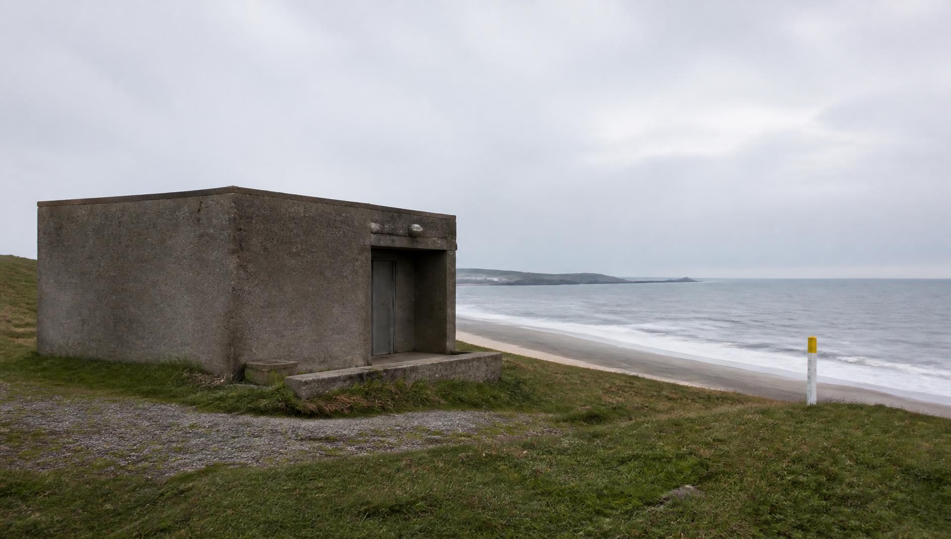 Schlichtes Betongebäude einer Kabellandestation an einer Küste mit Markierungspfosten am Strand