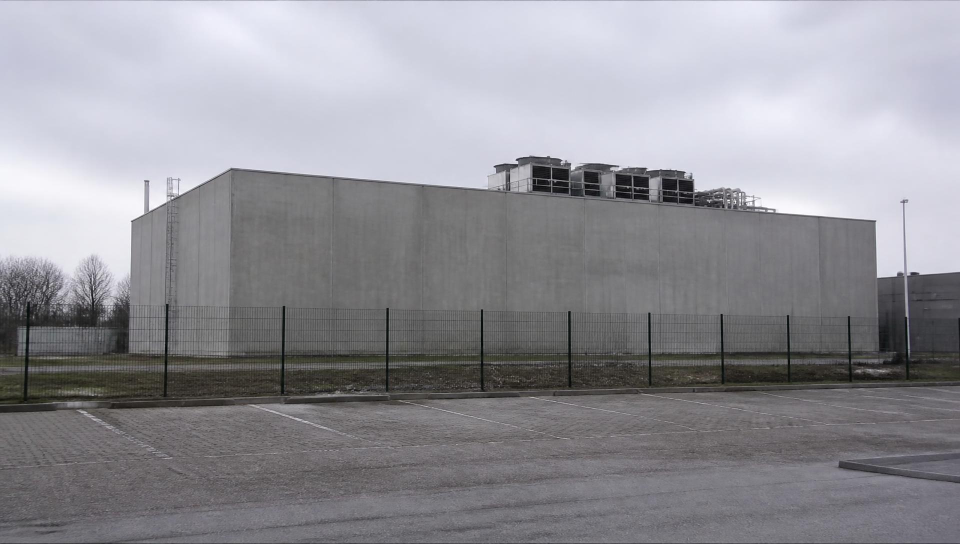 Fensterloses graues Betongebäude hinter einem Zaun – von außen ein gewöhnlicher Gewerbebau